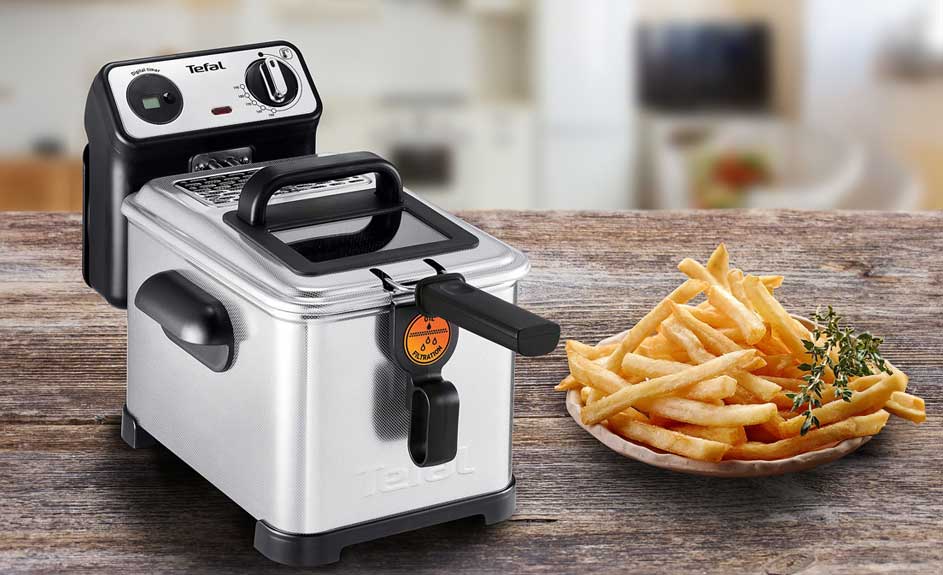 Une friteuse en métal près d'une assiette de frites sur une table en bois.