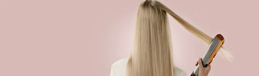 Vue arrière de longs cheveux blonds lissés avec un fer à lisser sur un fond rose pâle.