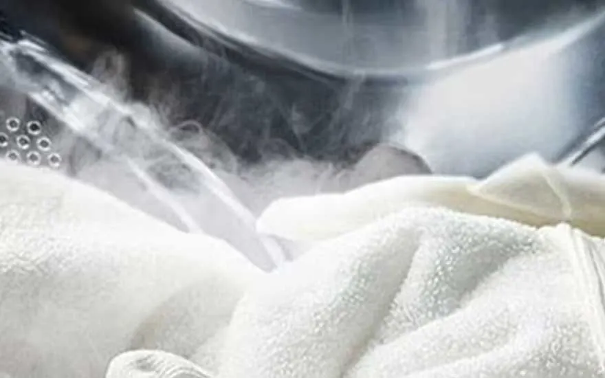 A close-up of steam or water mist inside a washing drum, focusing on white towels and a gentle, refreshing clean.