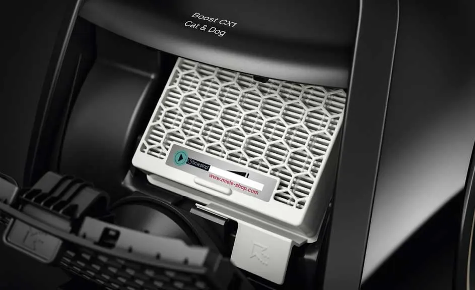 Un filtre blanc avec une grille hexagonale dans un aspirateur noir "Boost CX1 Cat & Dog". Une étiquette est visible.