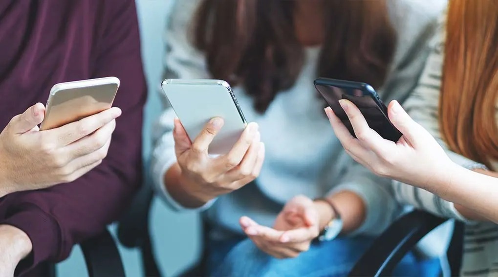 Trois personnes assises tenant des smartphones argentés, blancs et noirs. Les mains sont visibles.