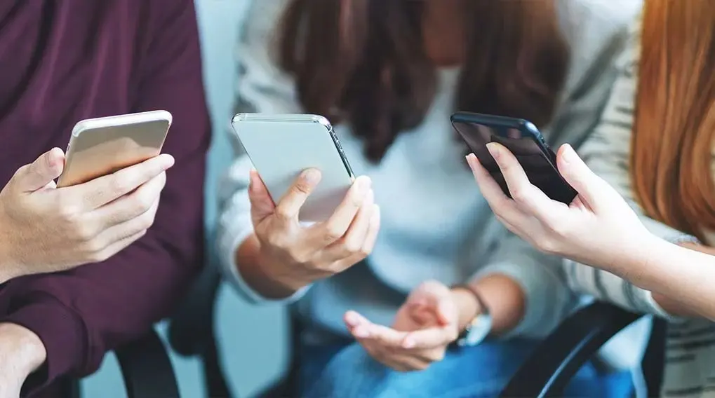 Trois personnes assises tenant des smartphones argentés, blancs et noirs. Les mains sont visibles.