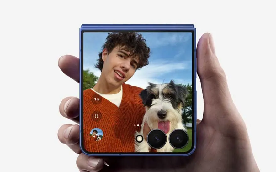 In een hand zie je een opgevouwen smartphone waarop een selfie van een jongen met een hond wordt weergegeven; heldere lucht op de achtergrond.