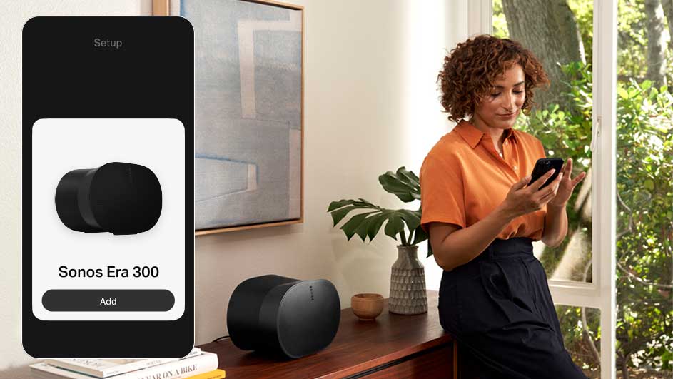 Een smartphone toont "Sonos Era 300" op het scherm. Een zwarte speaker staat op een houten dressoir naast een vaas en een plant.