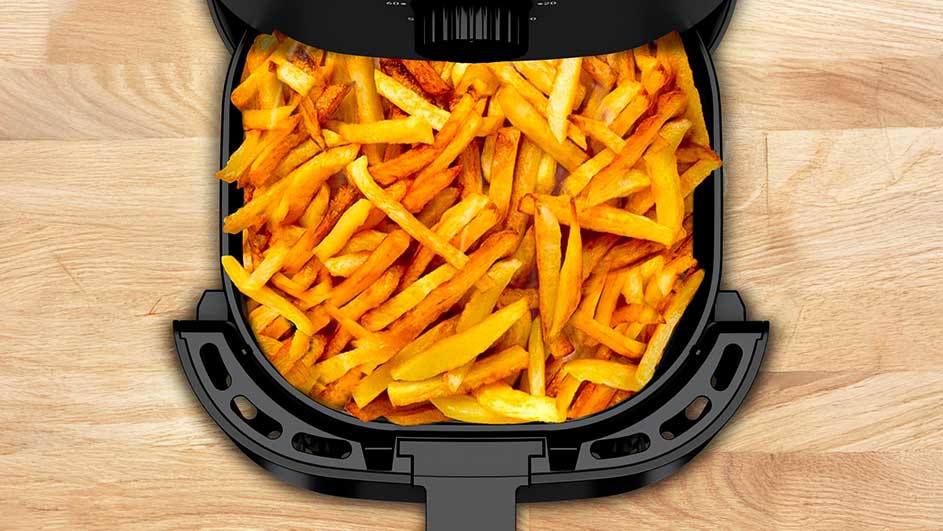 Friteuse noire remplie de frites dorées, sur un plan de travail en bois clair.