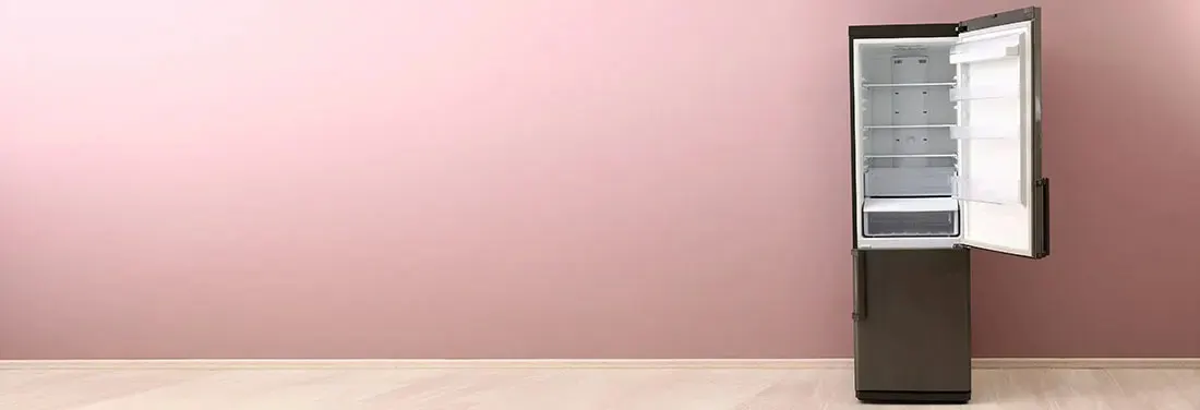 Réfrigérateur gris foncé avec porte ouverte, intérieur blanc, devant un mur rose sur un plancher beige.