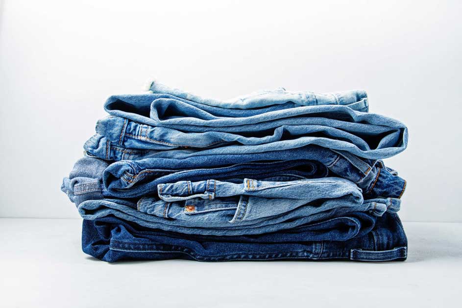 Pile de jeans bleus pliés sur un fond blanc. Les nuances de bleu varient.