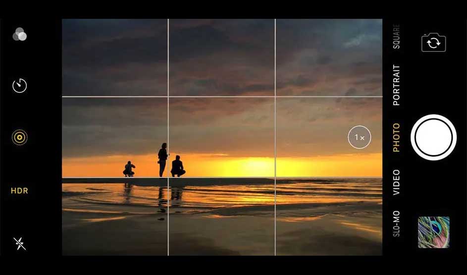 Zonsondergang gefotografeerd met een telefooncamera-interface, met rasterlijnen en camerabedieningselementen. Silhouetten op de horizon.