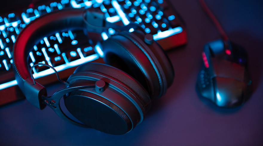 Un casque audio est posé devant un clavier lumineux bleu et une souris d'ordinateur sur une surface sombre.
