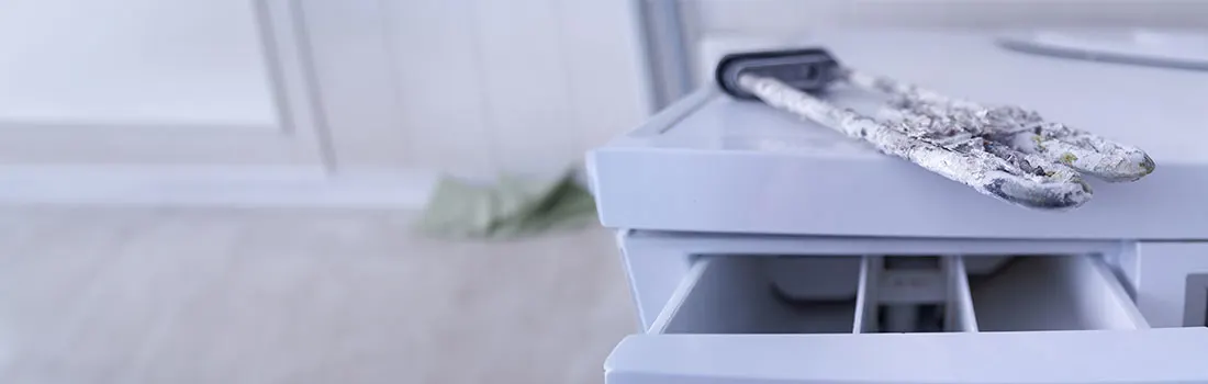 Une machine à laver blanche avec un tiroir ouvert et des gants blancs sales dessus.