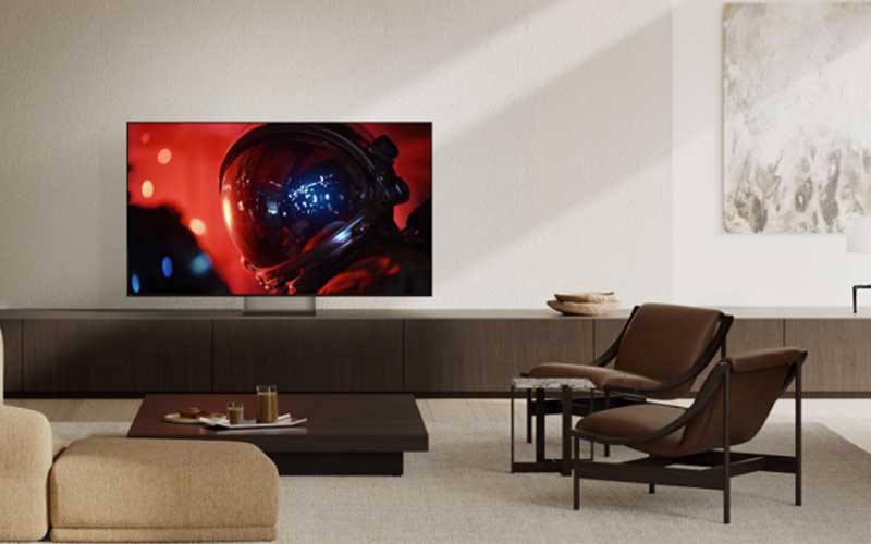Salon moderne avec une télévision murale montrant un astronaute, deux fauteuils bruns et une table basse.