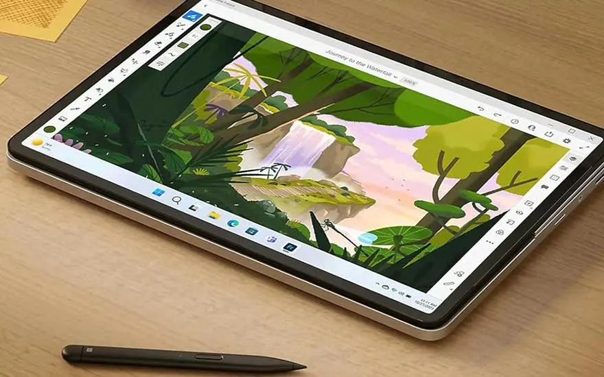 Tablette numérique affichant un dessin de paysage avec une cascade, un feuillage luxuriant et un ciel clair. Un stylet est posé à côté.