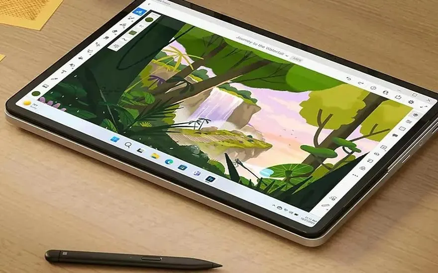 Tablette numérique affichant un dessin de paysage avec une cascade, un feuillage luxuriant et un ciel clair. Un stylet est posé à côté.