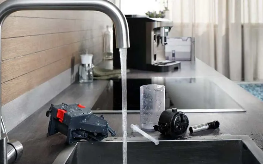 Een gootsteen met stromende kraan terwijl losse onderdelen van een koffiemachine zorgvuldig worden afgespoeld en gereinigd.