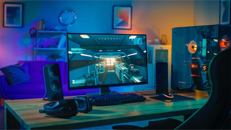 A gaming setup features a monitor displaying a sci-fi game, speakers, keyboard, headphones, mouse, and a gaming PC with visible fans.