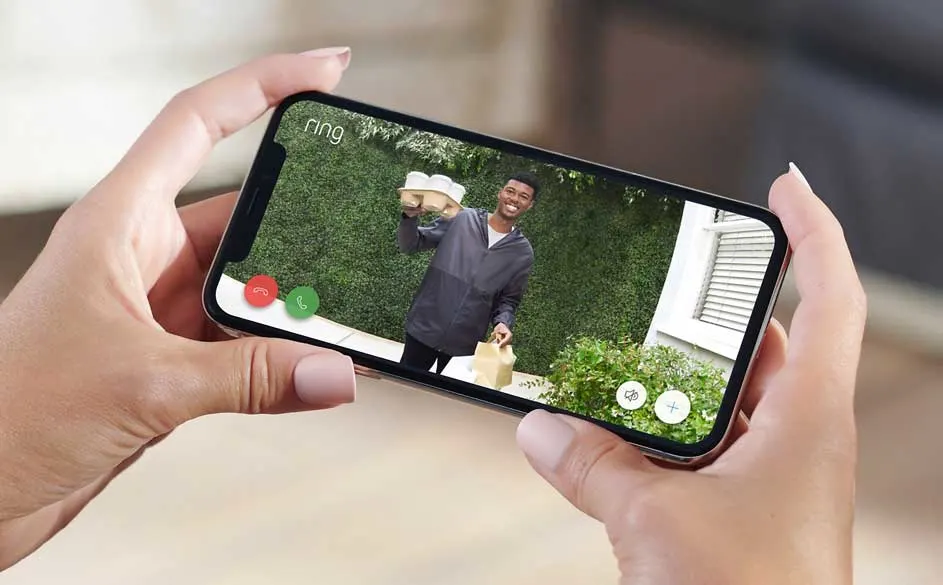 Een smartphone toont een Ring-videodeurbel met een persoon die pakketten vasthoudt voor een groene achtergrond.