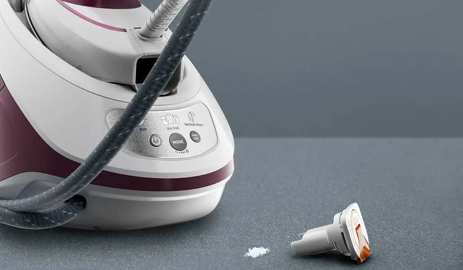 Een wit en bordeaux stoomstrijkijzer met een grijze slang, op een grijze achtergrond. Een klein wit onderdeel ligt ernaast.