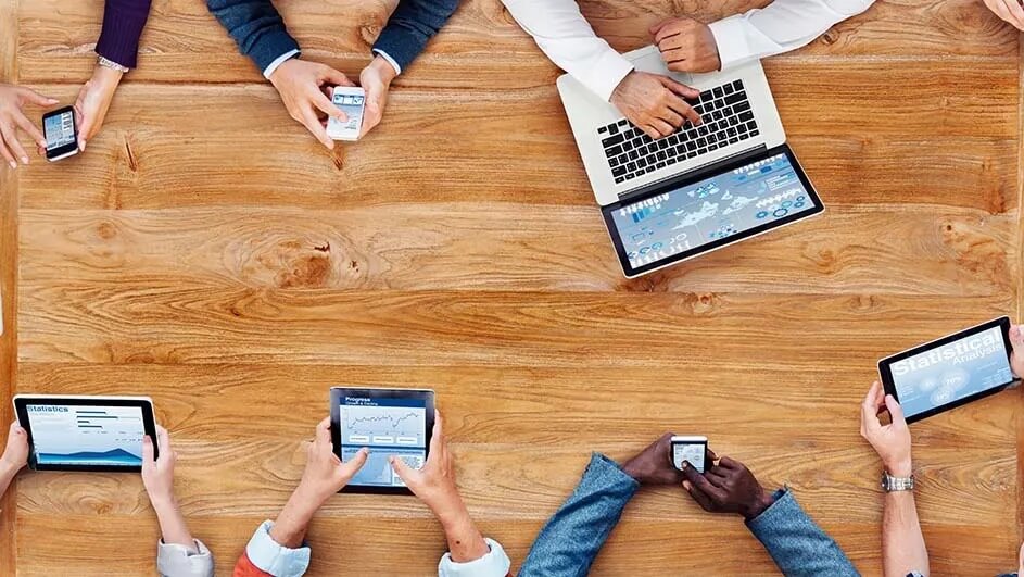 Overhead shot van een houten tafel met laptops, tablets en smartphones in gebruik.