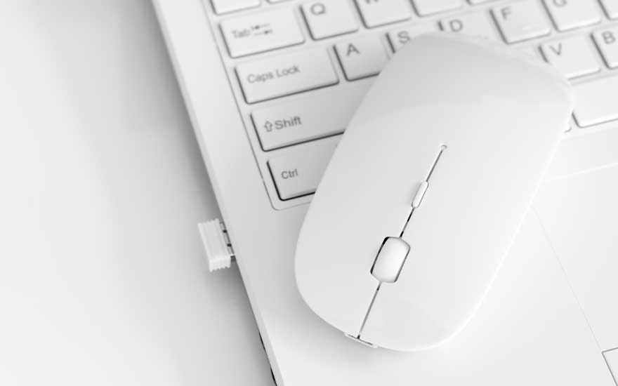 A white wireless mouse rests atop a white laptop, with visible keys and a USB receiver plugged into the side.