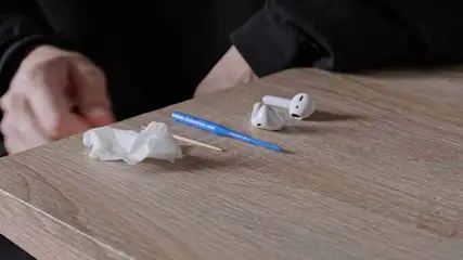 Sur une table en bois, il y a des écouteurs blancs, un cure-dent, un mouchoir blanc et un outil de nettoyage bleu.