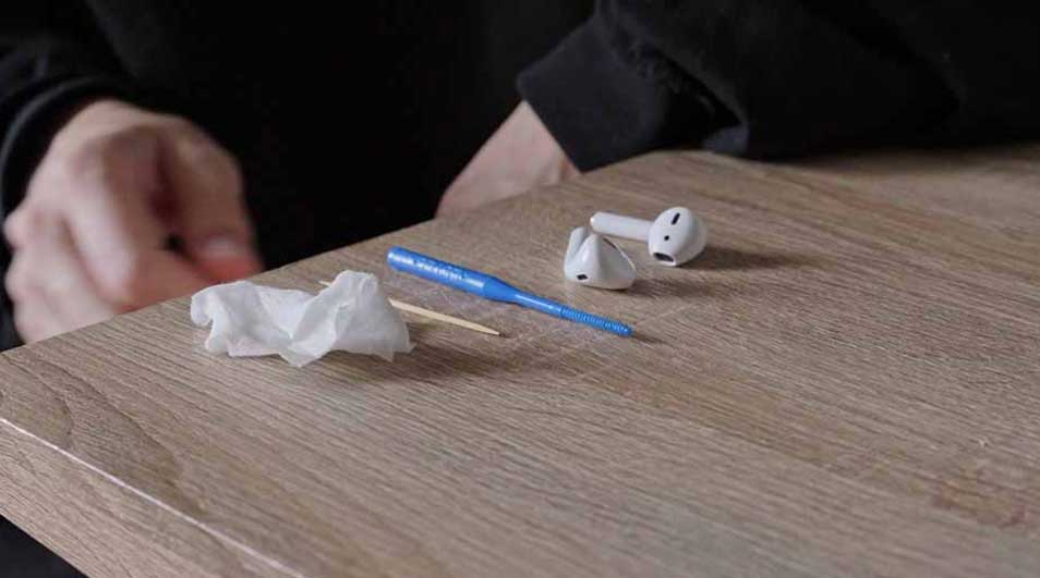 Sur une table en bois, il y a des écouteurs blancs, un cure-dent, un mouchoir blanc et un outil de nettoyage bleu.