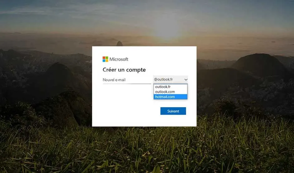 Fenêtre "Créer un compte" Microsoft sur fond de paysage montagneux et herbeux. Options de domaine de courriel visibles.