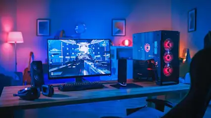 Een gamingopstelling met een blauw verlicht scherm, toetsenbord, luidsprekers en een pc-toren met rode ventilatoren op een houten bureau.