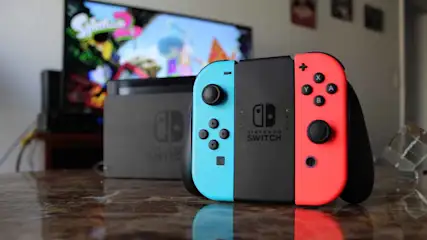 Een Nintendo Switch-console met blauwe en rode Joy-Con staat voor een tv met het spel Splatoon 2, in een woonkamer.