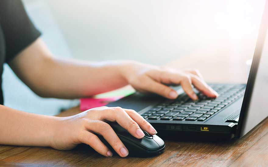 Mains sur un ordinateur portable noir avec souris sur une table en bois, fond clair.