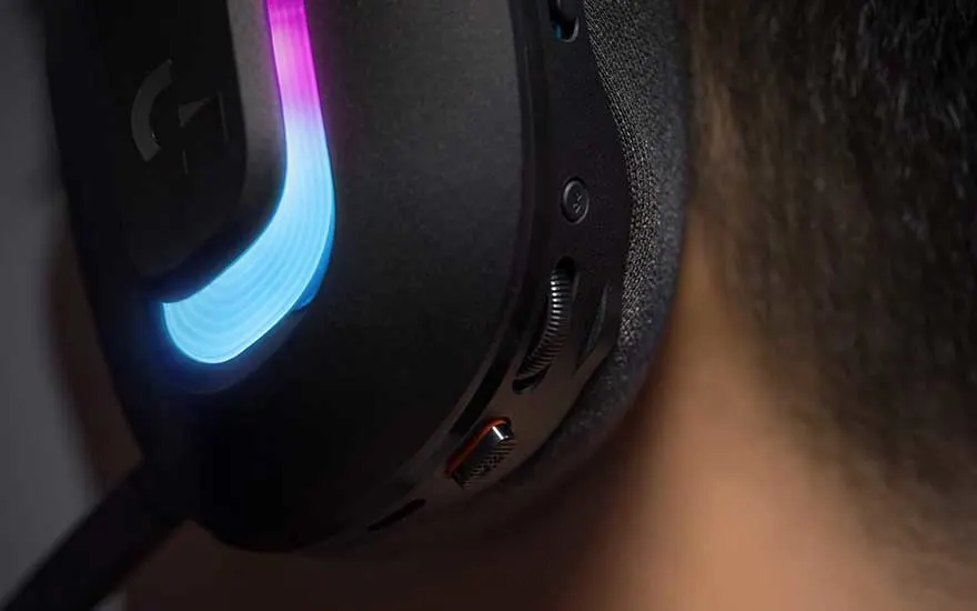 Close-up van een zwarte gaming headset met blauwe RGB-verlichting gedragen door iemand, met zichtbare bedieningsknoppen en microfoon.