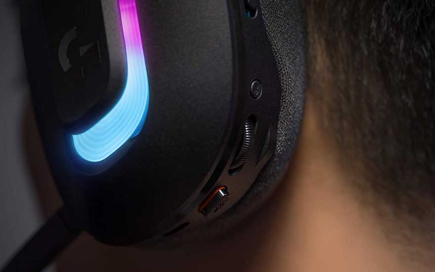 Gros plan d'un casque gaming noir avec éclairage RGB bleu porté par quelqu'un, montrant les boutons de contrôle et le microphone.