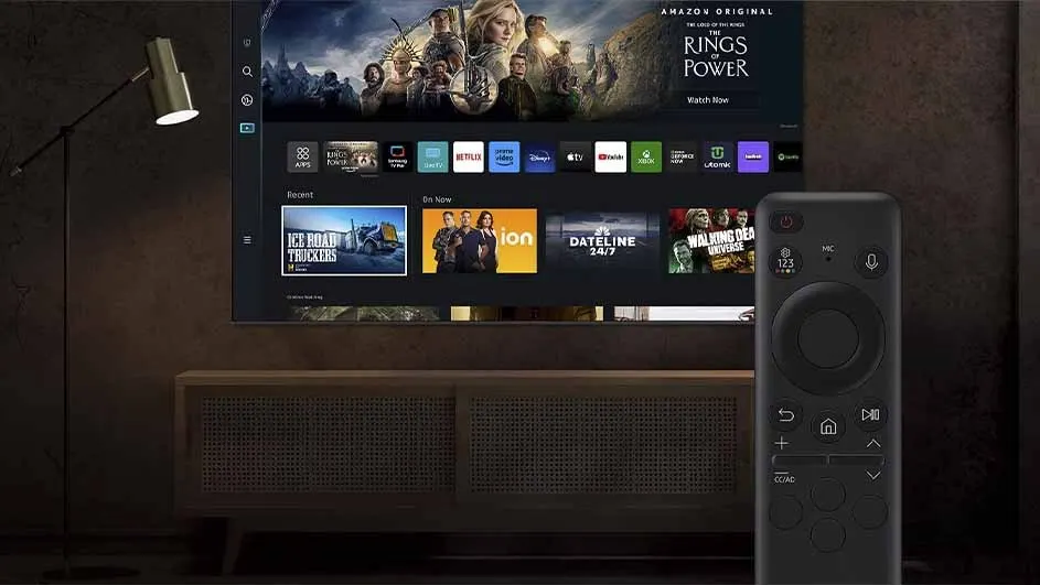 A television displays streaming apps and "Rings of Power". A remote control sits in front of a cabinet, near a lamp.