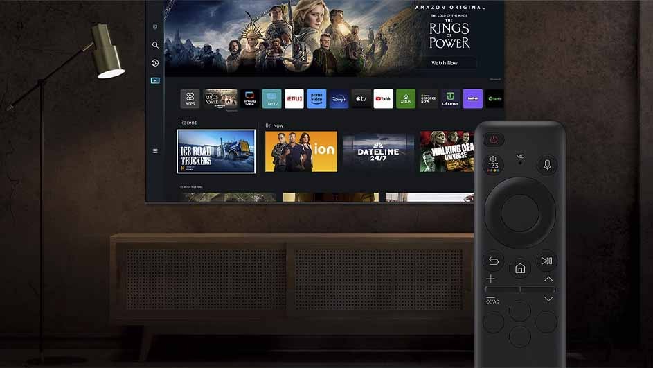 Een tv-scherm toont streaming-apps en 'Rings of Power'. Een afstandsbediening staat rechts. Een lamp staat links van de tv.