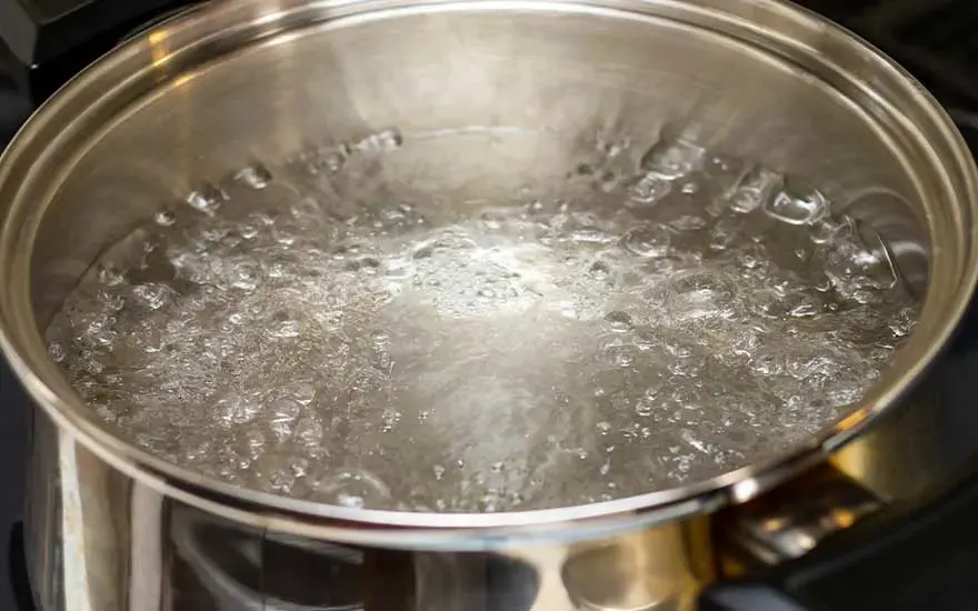 Eau bouillante avec de grosses bulles dans une casserole en métal sur la cuisinière, la marque n’est pas visible.