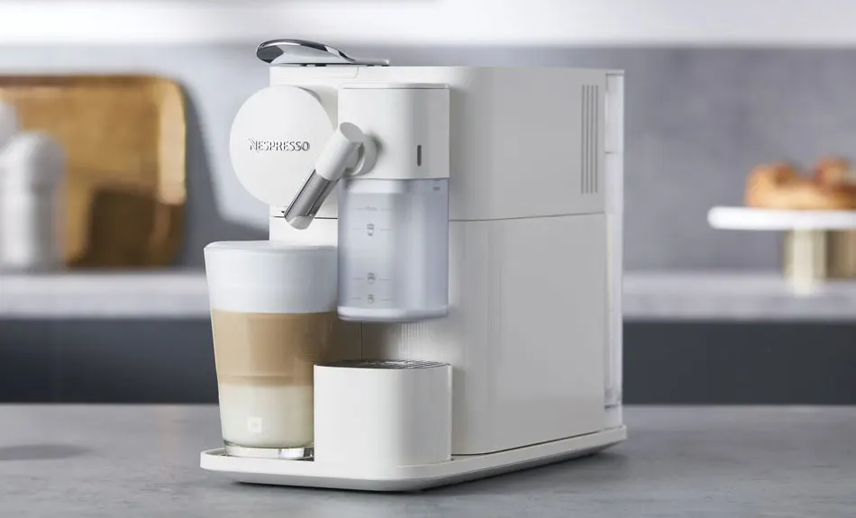 Machine à café blanche avec réservoir d'eau, tasse à café à trois couches, sur un comptoir de cuisine gris.