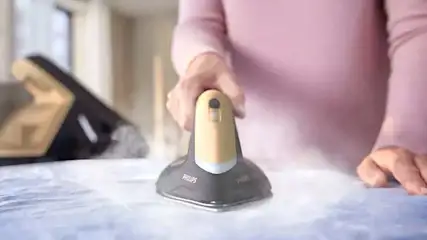 Een beige en grijze Philips stoomstrijkijzer wordt gebruikt op een blauw kledingstuk, met een ander strijkijzer in de wazige achtergrond.