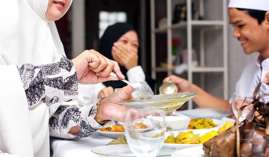 Une table avec des plats divers, des verres d'eau et des personnes en arrière-plan.
