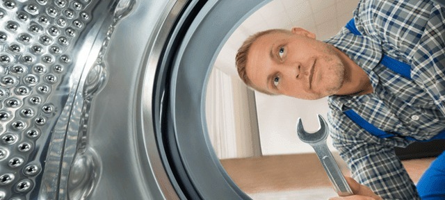 Een blik in een zilverkleurige wasmachine met een man met een moersleutel.
