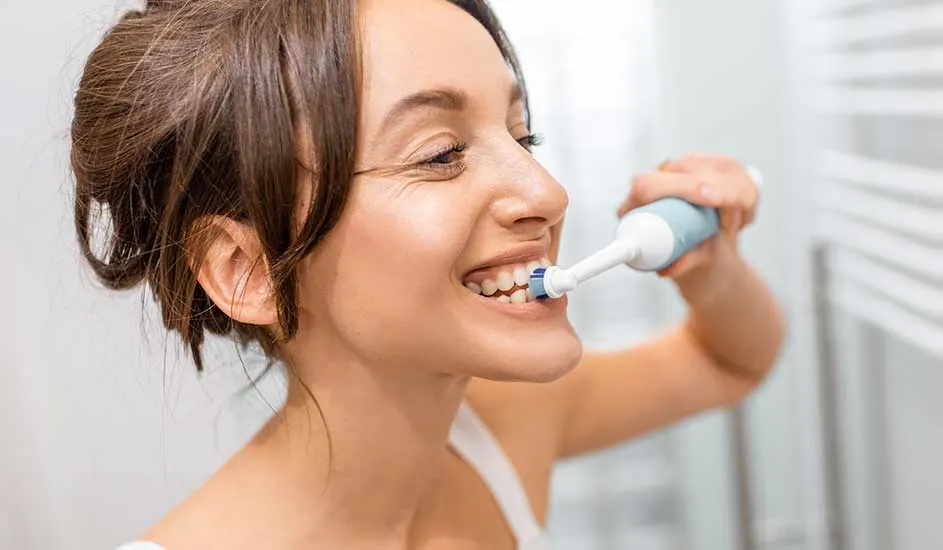 Une brosse à dents électrique blanche et bleue est utilisée pour nettoyer les dents. L'arrière-plan est blanc.