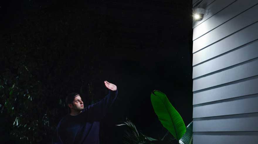 Buitenopname 's nachts: grijs huis met lamp, donkere tuin met groen blad.