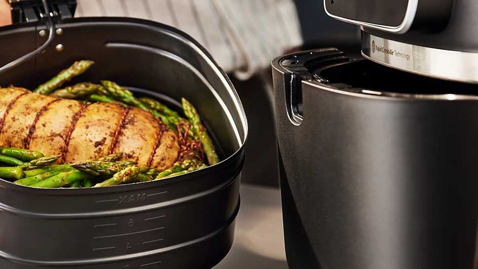Un panier noir contient du poulet rôti et des asperges vertes, à côté d'une friteuse à air noir.