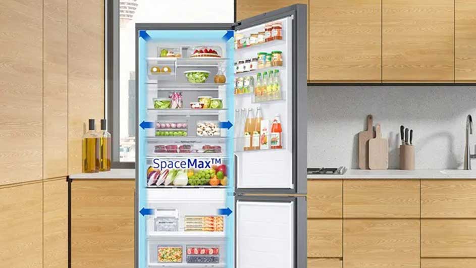 Un réfrigérateur gris ouvert montre des étagères remplies de nourriture. L'arrière-plan présente des armoires de cuisine en bois.