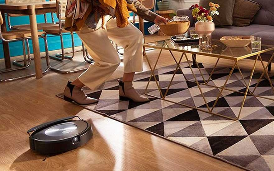 Aspirateur robot noir sur parquet clair près d'un tapis à motifs triangulaires sous une table basse dorée.