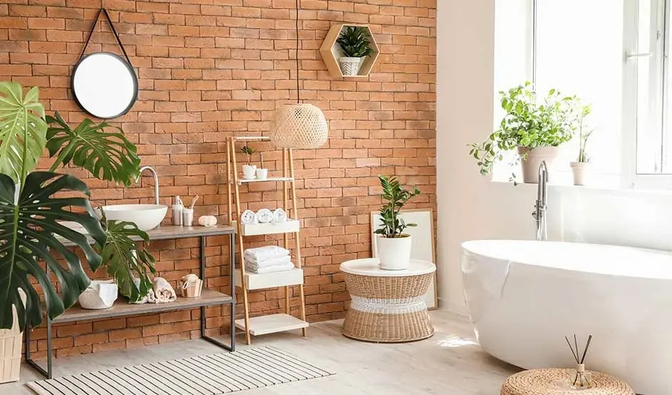 Een moderne badkamer met bakstenen muur, vrijstaand bad, veel groene planten en houten meubels. Merk: geen zichtbaar merk.