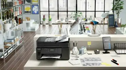 Een zwarte printer op een wit bureau met kantoorartikelen in een lichte ruimte met rekken en ramen.