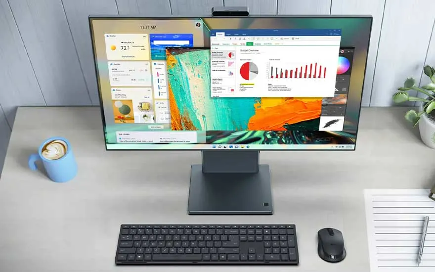 Een bureau met een computer, toetsenbord, muis, notities, pen, koffie en een plant. Op het scherm staan grafieken en info.