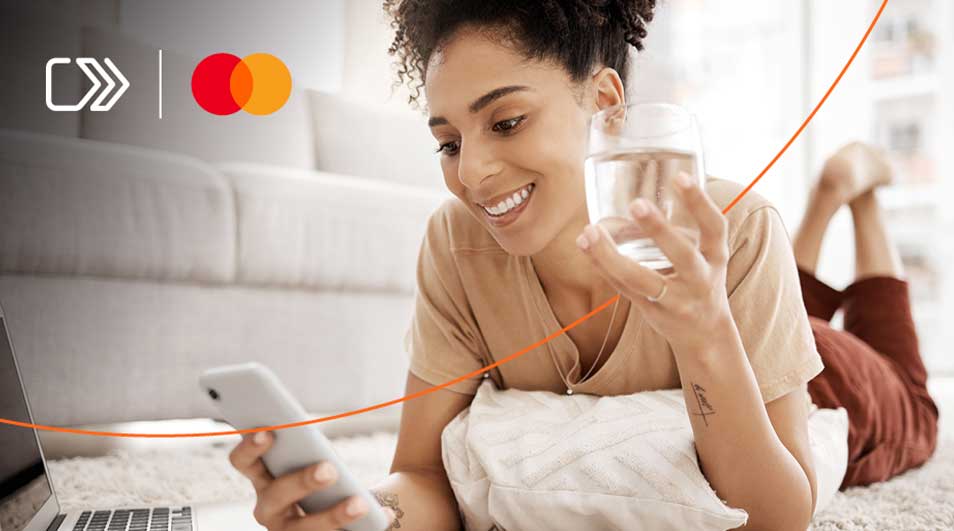 Une personne allongée sur un tapis, tenant un téléphone et un verre d'eau près d'un ordinateur portable et un canapé.