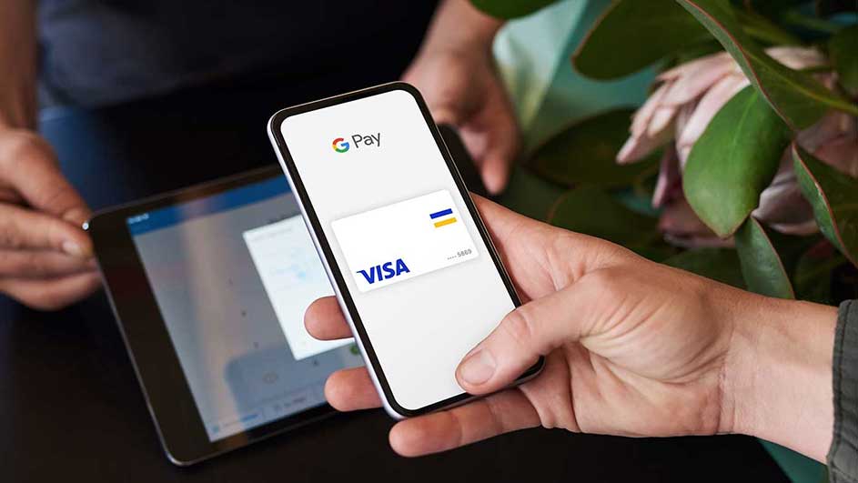 Een telefoon met Google Pay en een Visa-kaart wordt vastgehouden, naast een tablet en planten.
