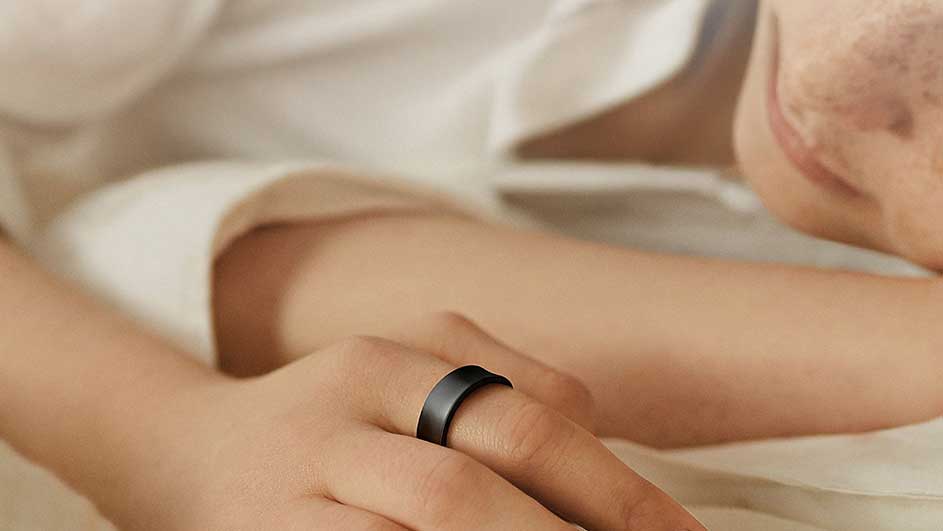 Zicht op een hand met een matzwarte ring om een vinger, tegen een achtergrond van een wit overhemd en huid.