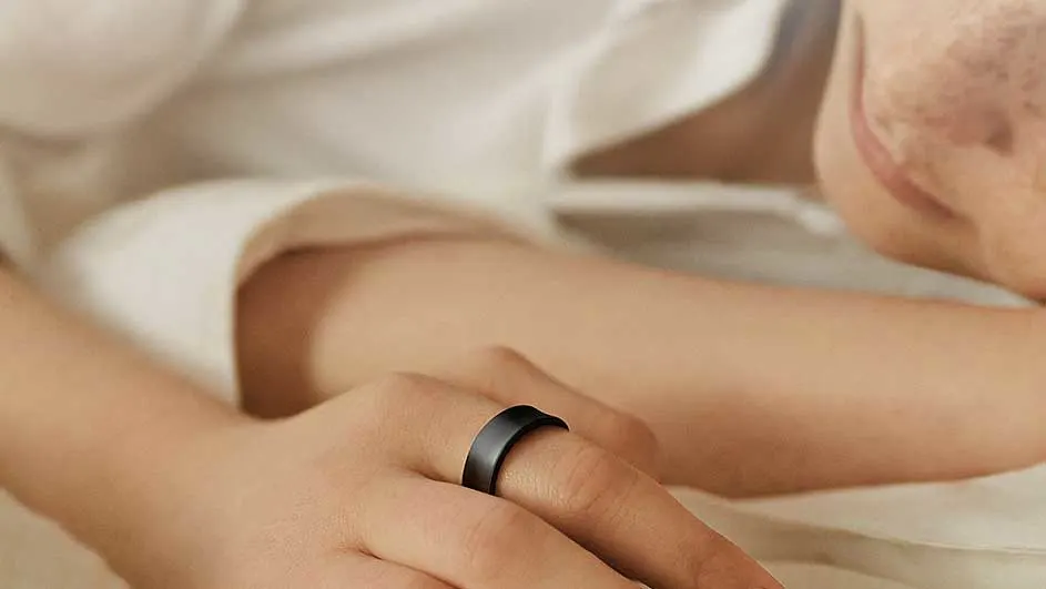 Zicht op een hand met een matzwarte ring om een vinger, tegen een achtergrond van een wit overhemd en huid.